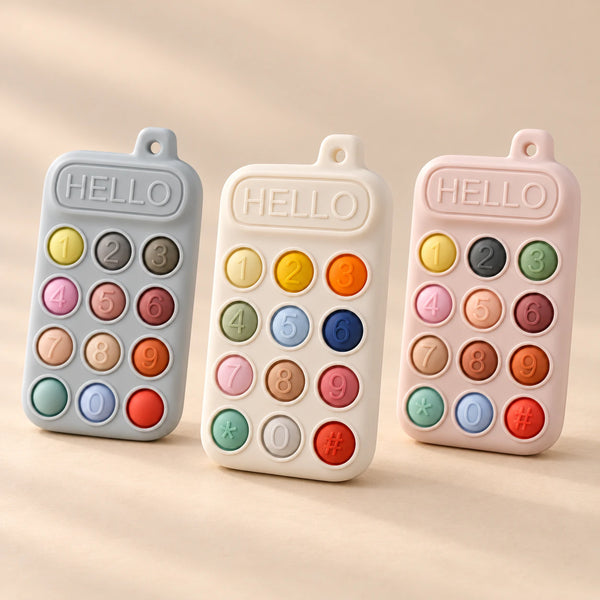 Click & Calm Silicone Phone Teether colour choices in Misty Grey, Vanilla Cream and Blush Pink on a warm beige studio background