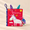 TibaToes Snuggle Stories Magical Unicorn cloth sensory book on a warm beige background.