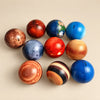 Ten planet-themed balls with eight planets, the Moon and a standard Sun on a warm beige studio background.