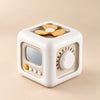 TibaToes Montessori Busy Cube in Off White/Yellow, showing its visible activity panels on a warm beige background.