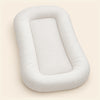 Empty cream SnuggleNest lounger with a rounded padded perimeter and inset centre, shown alone on warm beige.