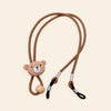 Brown cord with bear charm, sliding bead and two adjustable black end loops on a warm beige background.