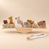 A wooden animal balance set on a straight plank and semicircular rocker, with a cotton threading cord in warm daylight.