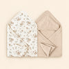 Two hooded towels, one white with brown floral print and one plain oat beige. Shown on warm beige.