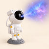 White astronaut galaxy night light projector on an oak bedside table with its blue and violet nebula effect visible on the textured wall.
