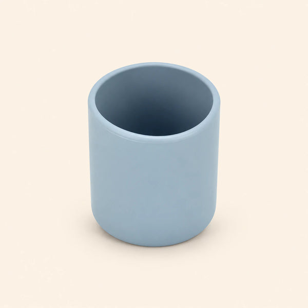 Grey blue open silicone training cup with a smooth rounded rim on warm beige.