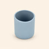 Grey blue open silicone training cup with a smooth rounded rim on warm beige.