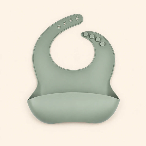 Sage Green silicone catch bib, with a scoop pocket and adjustable button-and-hole neck closure, on warm beige.