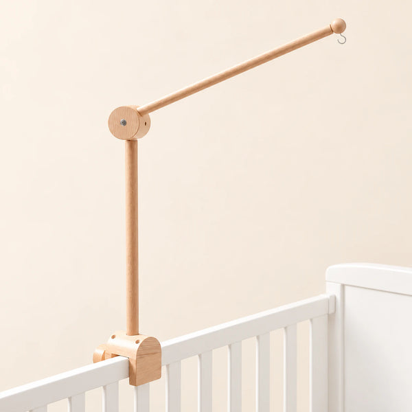 Natural wooden mobile arm with a round hinged joint, small hanging hook and clamp mounted on a white crib rail.