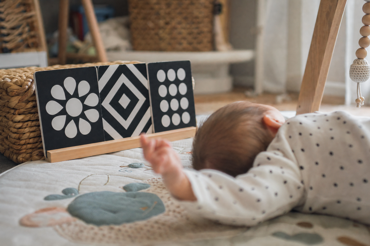 High-contrast black-and-white baby cards propped beside a young baby lying on a play mat, seen from behind