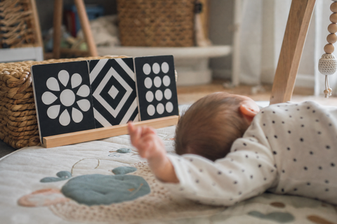 High-contrast black-and-white baby cards propped beside a young baby lying on a play mat, seen from behind