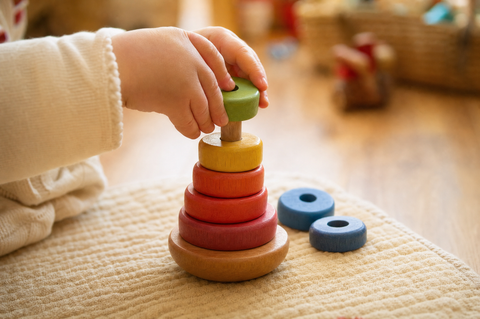 Toddler hands placing a colorful wooden ring onto a wooden stacking tower on a play mat