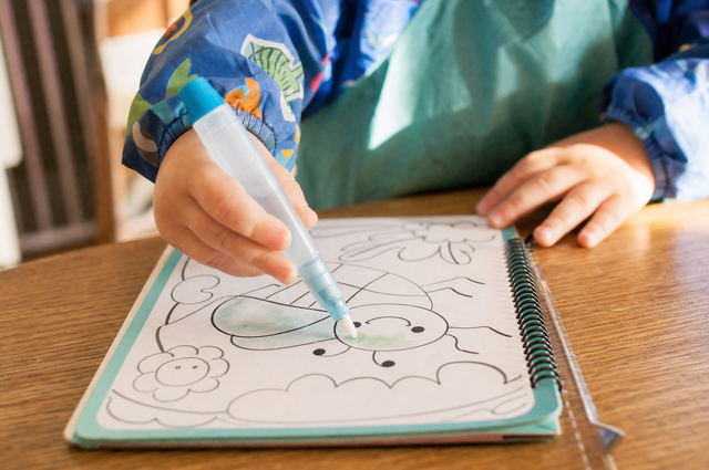 Young child's hands using a water pen to color a reusable coloring book page on a wooden table