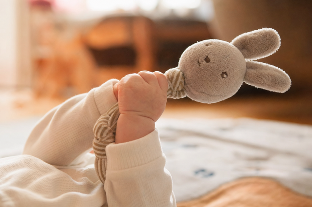 A young baby's tiny hands gripping a soft plush rattle toy on a play mat
