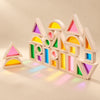 Rainbow building blocks with wooden-style frames and transparent coloured panels arranged on a warm beige studio surface.