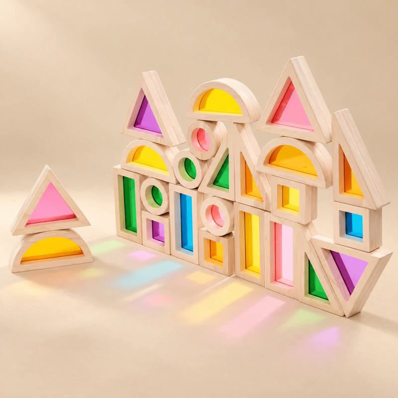 Rainbow building blocks with wooden-style frames and transparent coloured panels arranged on a warm beige studio surface.