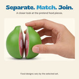 Original close photograph of an adult hand holding two green toy fruit halves apart, showing the circular fasteners inside. Food designs vary by set.