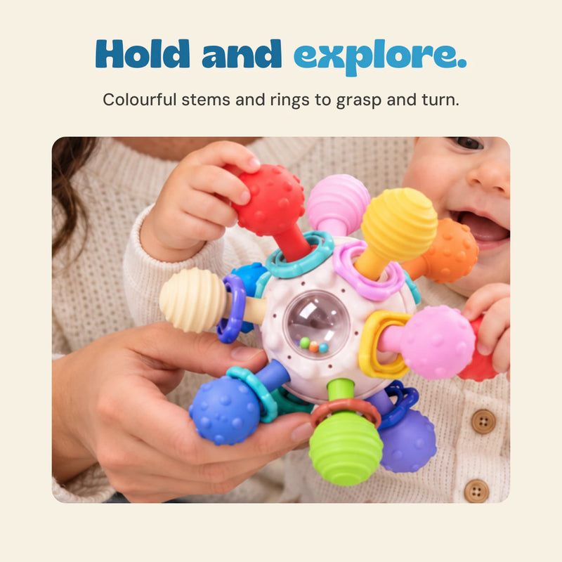 Close view of a baby and adult holding the sensory ball, with its textured coloured ends, rings and clear bead window.