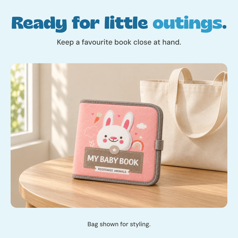 Closed pink bunny My Baby Book on an oak table beside a cream tote bag in natural light.