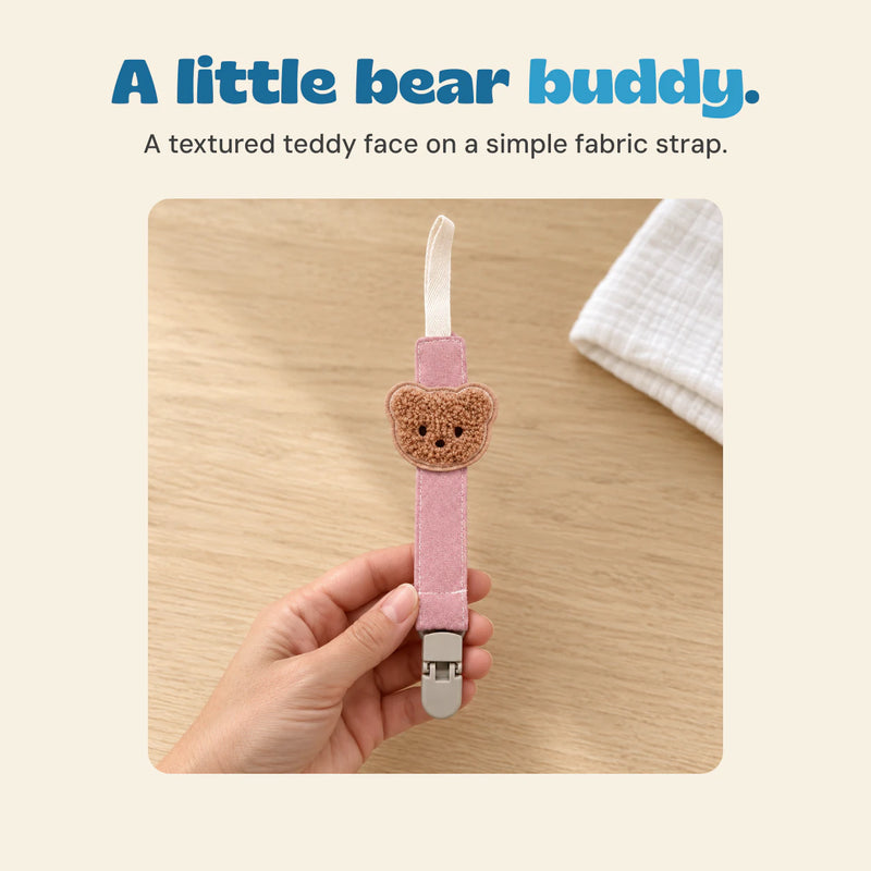 Adult hand holding the pink Bear Buddy clip, with its full cream loop, brown teddy detail and grey clasp visible.