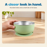 An adult hand steadies the sage bowl, showing its rounded outer shell, metal interior and small base tab.