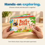 Adult hands hold the farm-themed Busy Book above a light wood table.