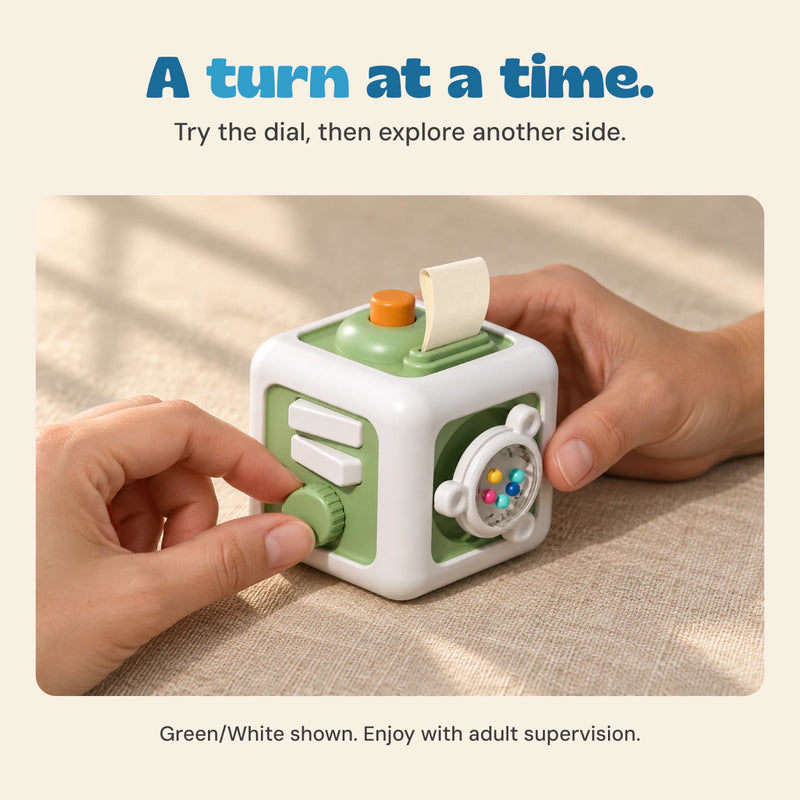 Adult hands gently turn the ridged dial on the Green/White TibaToes Busy Cube.