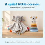 The grey elephant snuggle blanket and six-ring koala stacking tower sit on a pale oak shelf in a calm home setting.