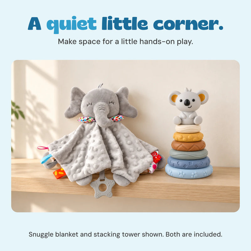 The grey elephant snuggle blanket and six-ring koala stacking tower sit on a pale oak shelf in a calm home setting.