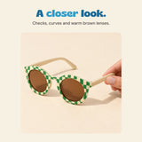 An adult hand holds the Green option, showing its green and cream checked frame and brown lenses.