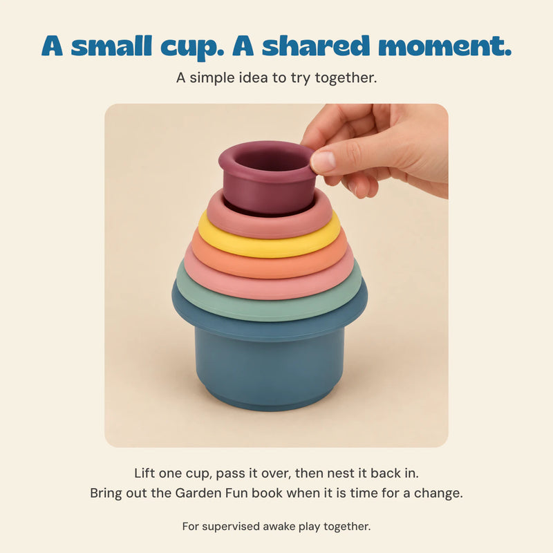 Adult hand lifting the smallest burgundy Earth Tone cup from the nested set, with a simple shared-play idea.