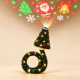 Green Christmas tree projector with glowing fairy lights, red baubles and a curved ring base, with festive light patterns visible on a light beige background.