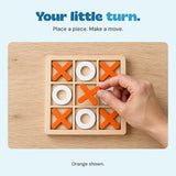 An adult hand holds an orange cross over the empty centre square of the wooden board.