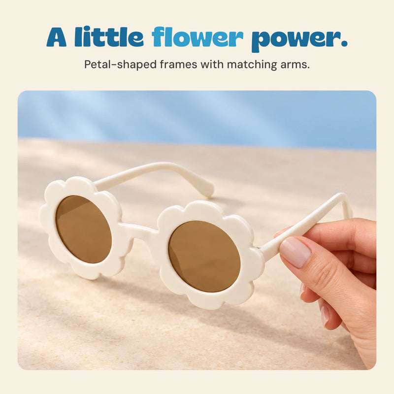 An adult hand holds white flower-shaped sunglasses, showing the matching arms and brown round lenses.