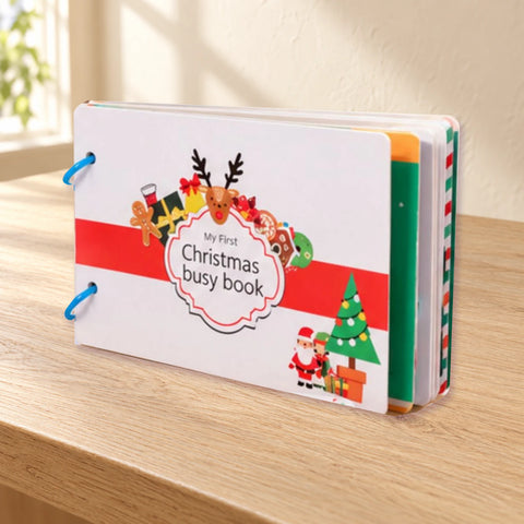 Photographed Christmas busy book with a red band, festive cover illustrations and blue binding rings, isolated on warm beige.