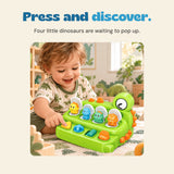 A child presses the yellow button on the green dinosaur toy, with four colourful dinosaurs visible in open compartments.