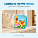 Closed dinosaur activity book standing beside a plain canvas bag in a quiet entryway.