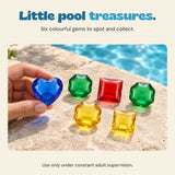 An adult hand holds the blue heart gem beside a pool, with the other five colourful gems on the coping. Six-gem set shown. Use only under constant adult supervision.