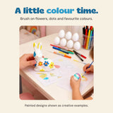 Original hands-on scene showing the ceramic bunny, eggs, colouring pens and a brush used for Easter painting.