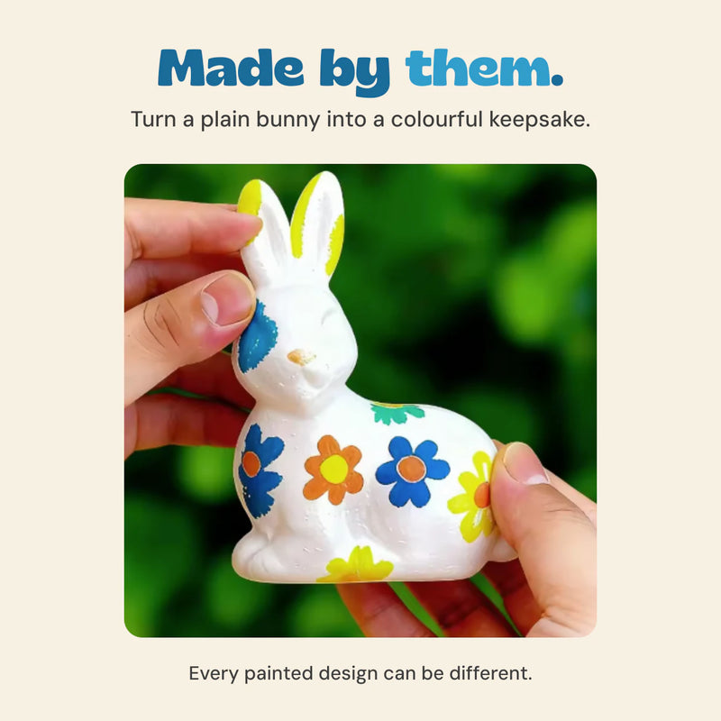 Original close-up of hands holding the ceramic bunny decorated with blue, orange and yellow flowers.