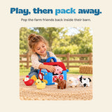 A child places the pink soft pig into the blue barn bag, with the other farm animal toys on the picnic mat.
