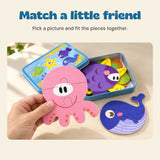 An adult hand holds the pink octopus puzzle beside its blue storage tin and matching sea-animal puzzles.