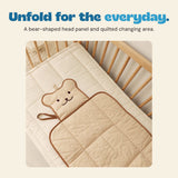 The beige bear changing mat opened on a padded surface, showing brown trim and quilted fabric.