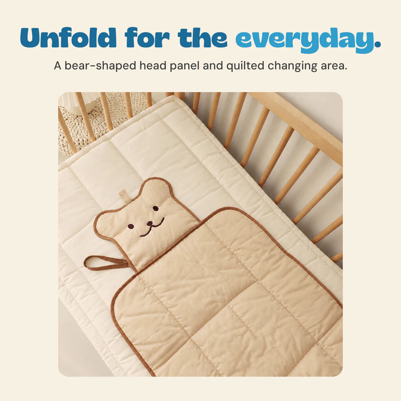 The beige bear changing mat opened on a padded surface, showing brown trim and quilted fabric.