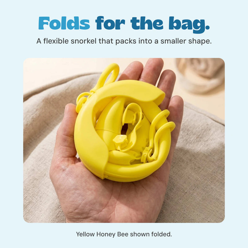 Original product photograph of a yellow snorkel folded into a compact shape in an adult hand.