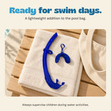 Blue foldable snorkel and matching cover resting on a towel beside a cream pool bag.