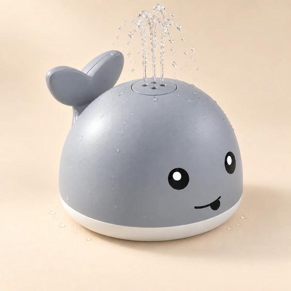 Pebble Grey whale toy spraying a gentle clear-water fountain on a warm beige studio background.