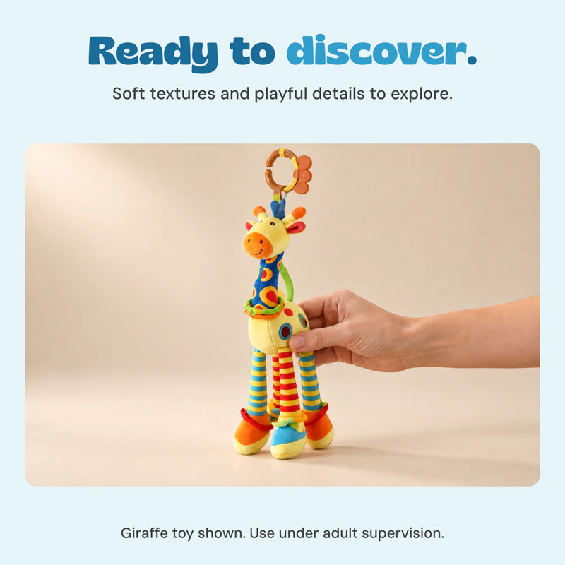 An adult hand holds the included giraffe toy above a wooden table in a warm naturally lit room.