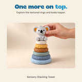 An adult hand places the koala topper onto the included textured stacking rings.