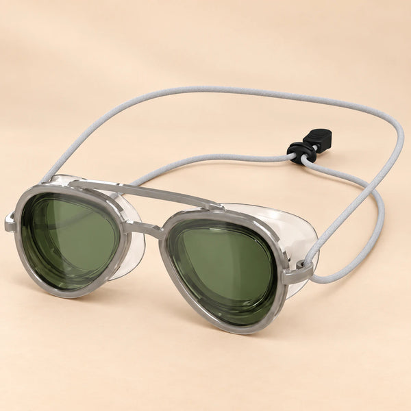 SplashView swim goggles in Sea Green with clear frames and adjustable cord, on a warm beige studio background.